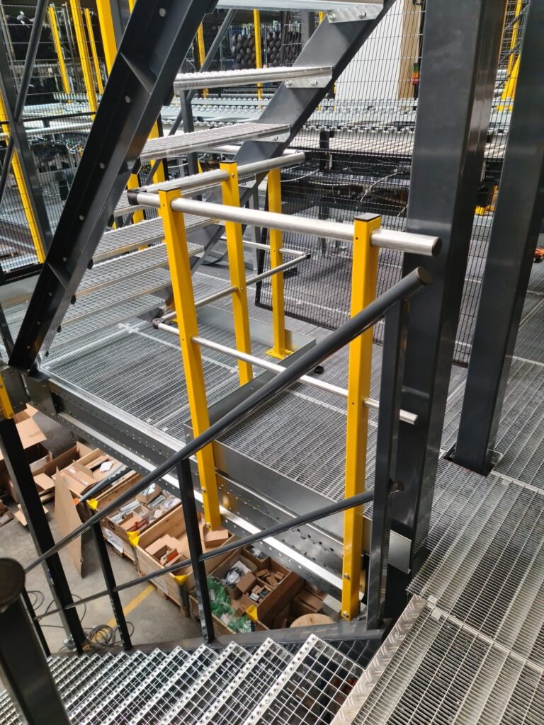 Entresolvloer op maat met stalen roostervloer, trap en gele leuning in magazijn