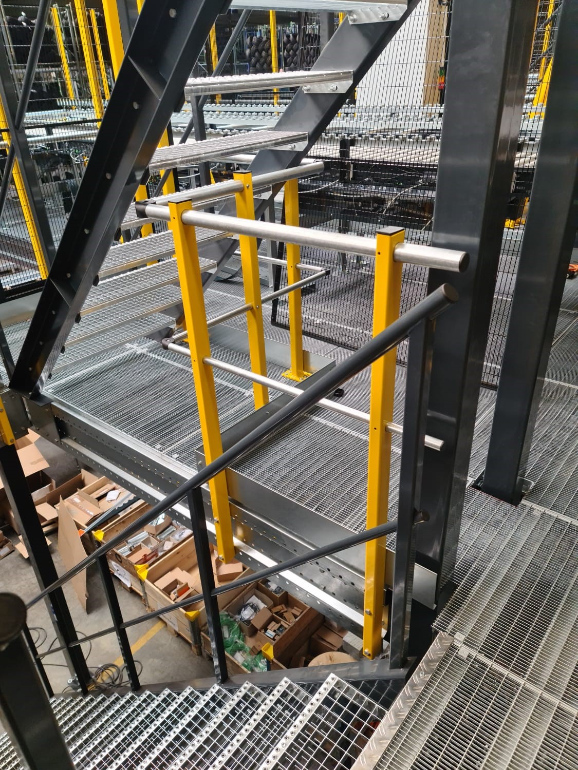 Entresolvloer op maat met stalen roostervloer, trap en gele leuning in magazijn