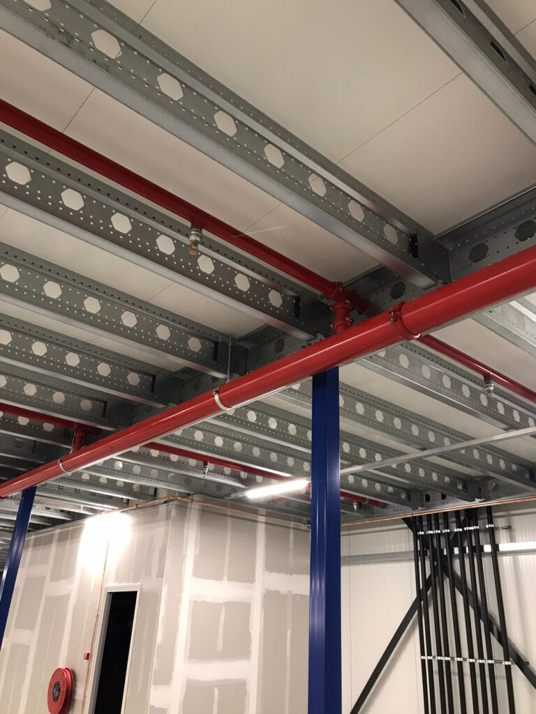 Mezzanine vloer op maat met stalen constructie, blauwe kolommen en rode brandleiding in bedrijfshal