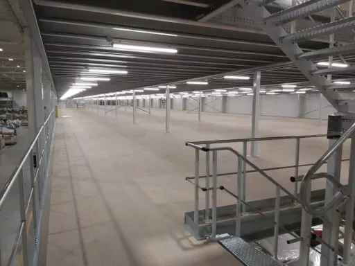 Grote entresolvloer met metalen trap en ondersteunende kolommen, geschikt voor extra opslagruimte in magazijn.