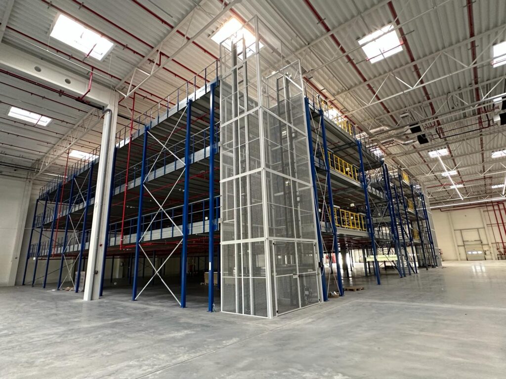 Mezzanine vloer op maat in magazijn met stalen constructie, meerlaagse platformen, trap en gele leuningen