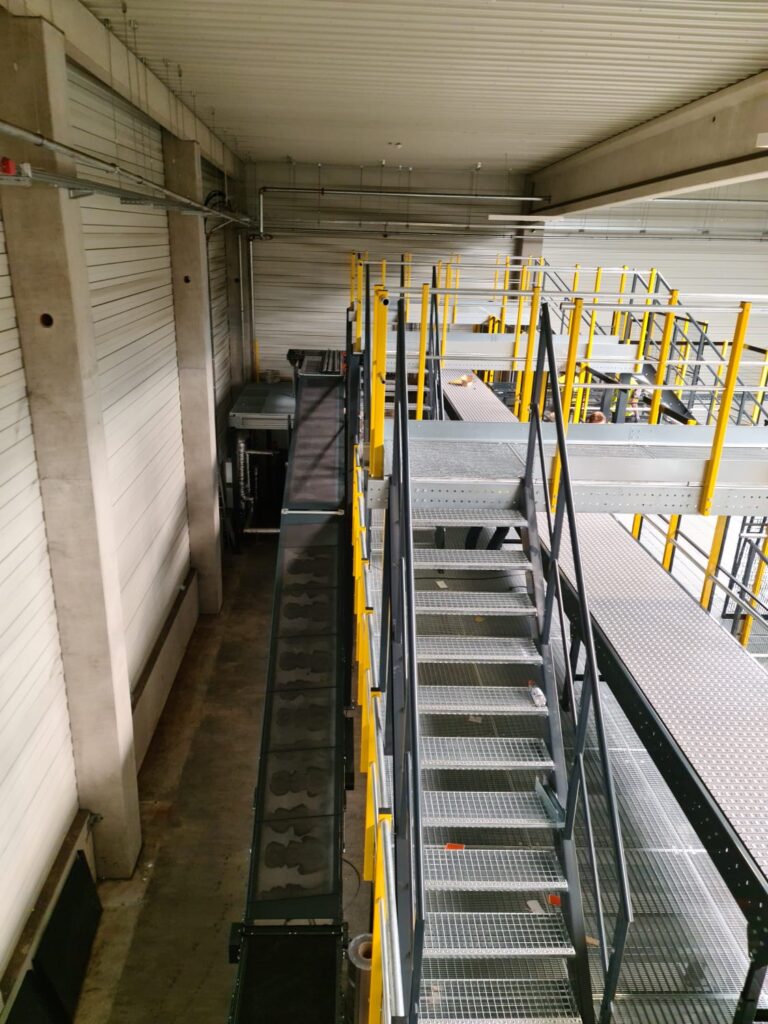 Mezzanine vloer stalen constructie met trap en gele leuningen op maat voor magazijn