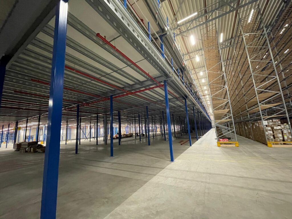 Mezzanine vloer op maat met blauwe stalen kolommen, vloerplaten en rekken in magazijn