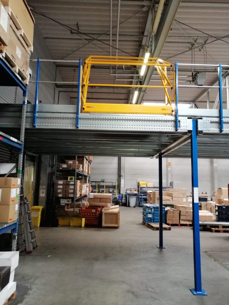 Mezzanine vloer op maat, stalen constructie met metalen vloerplaten en geel veiligheidshek in magazijn