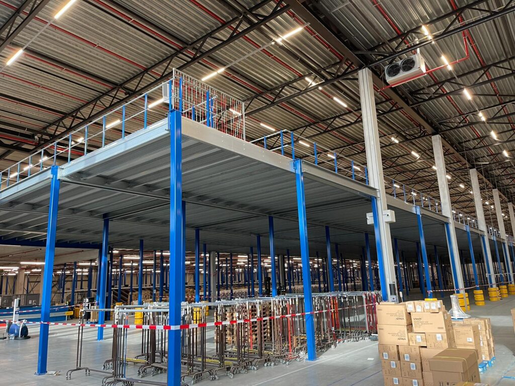 Mezzanine vloer op maat met staalconstructie, blauwe kolommen en trap in magazijn